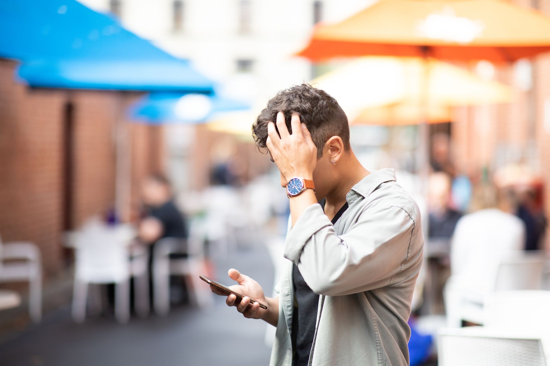 Young handsome Latin man looking at the smartphone with his stress and wondering face expression. He is trying to look for the place and he could't find it concept.Blurred market outdoor background